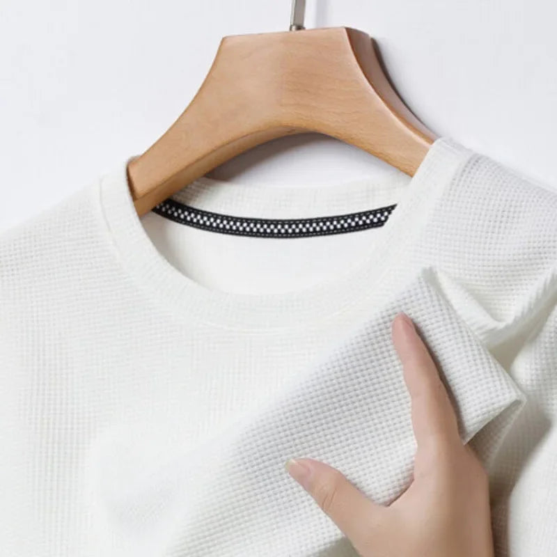 White textured sweater on a wooden hanger with a hand touching the fabric.