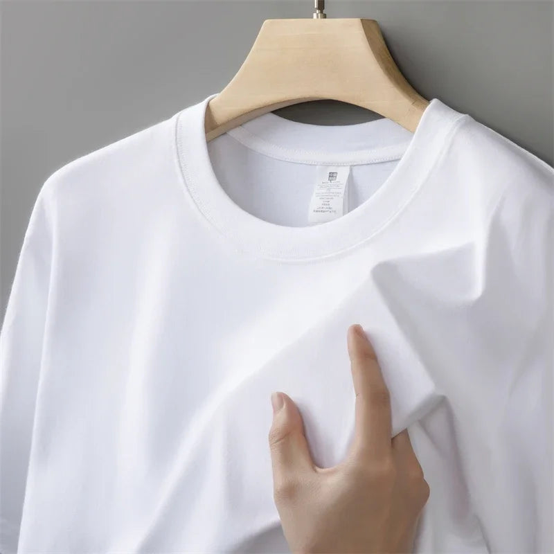 White t-shirt on a wooden hanger with a hand touching it against a gray background