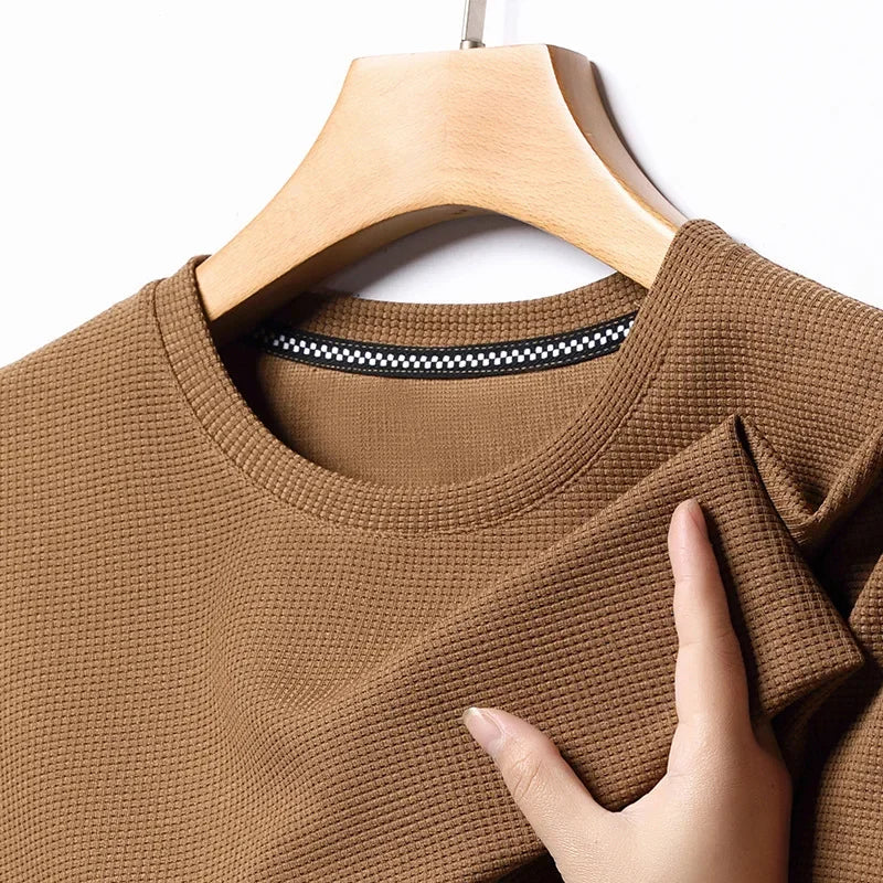 Brown textured sweater on a hanger with a hand touching the fabric