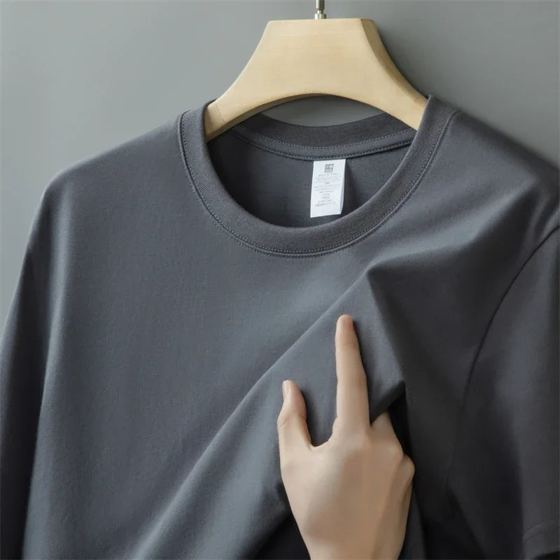 Gray t-shirt on a hanger with a hand touching the fabric against a gray background