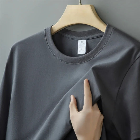 Gray t-shirt on a hanger with a hand touching the fabric against a gray background