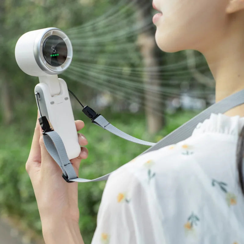 Person using a handheld device with a strap, possibly a sprayer or fan, outdoors.