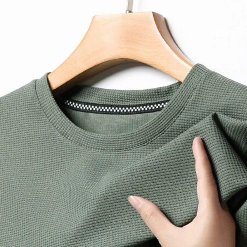 Green textured sweater on a hanger with a hand touching the fabric
