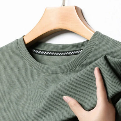Green textured sweater on a hanger with a hand touching the fabric